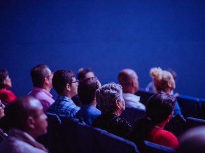 An attentive group of adults seated at an indoor conference, focusing on a presentation.