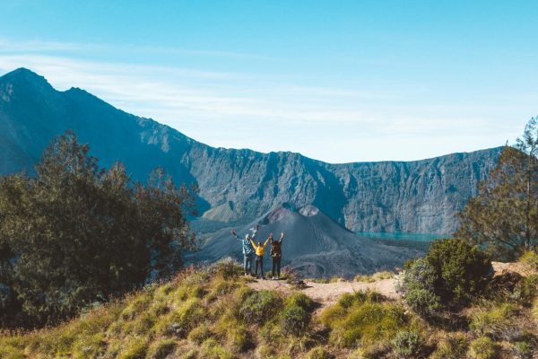 Three hikers raise their arms in joy at the crater rim of Mount Rinjani, Lombok, Indonesia.