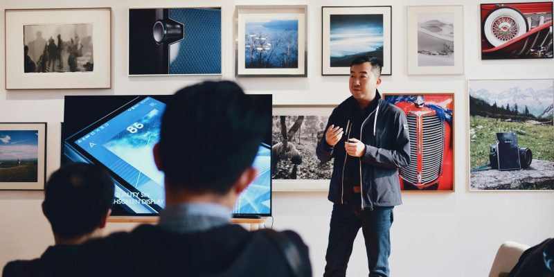 Man giving a presentation in a modern art gallery setting, engaging audience.